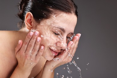 Attractive woman washing her face on grey background, space for text