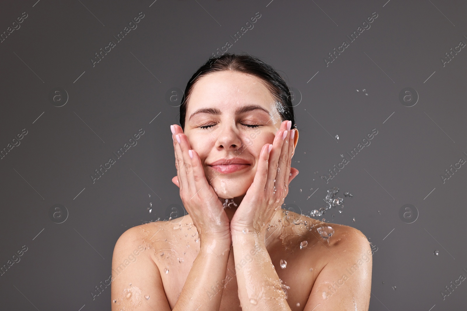 Photo of Attractive woman washing her face on grey background