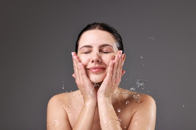 Attractive woman washing her face on grey background