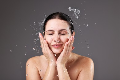 Photo of Attractive woman washing her face on grey background