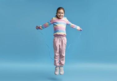 Photo of Cute little girl with jump rope on light blue background