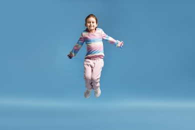 Photo of Cute little girl with jump rope on light blue background