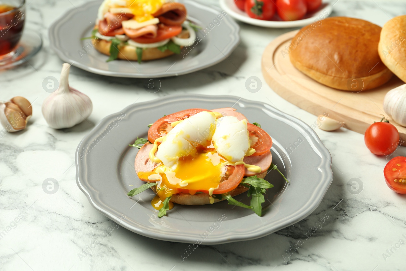 Photo of Tasty brunch. Poached egg, ham, tomato, arugula and bun on white marble table, closeup