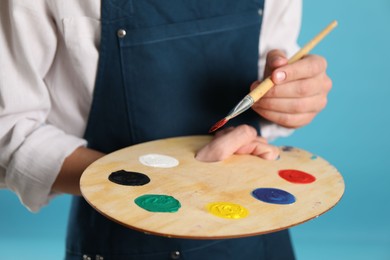 Photo of Man with wooden palette and paintbrush on light blue background, closeup