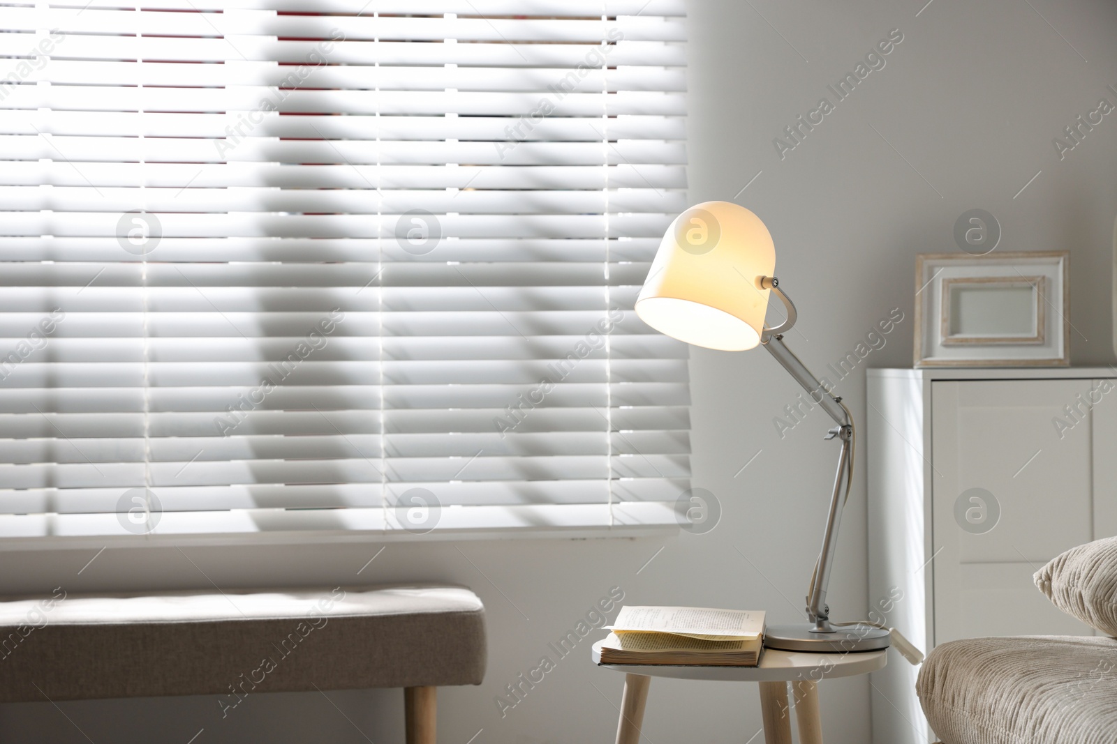 Photo of Stylish night lamp and book on side table near window in room. Interior design