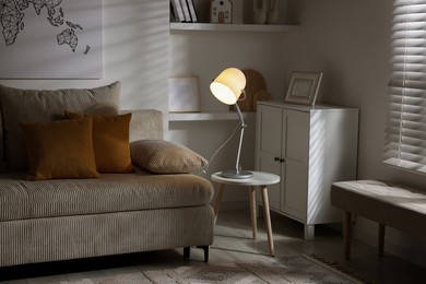 Photo of Stylish night lamp on side table near sofa in room. Interior design