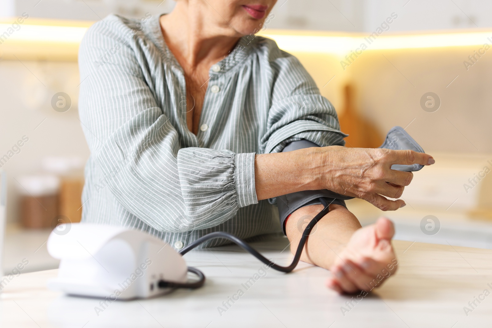 Photo of Senior woman measuring blood pressure at table in kitchen, closeup