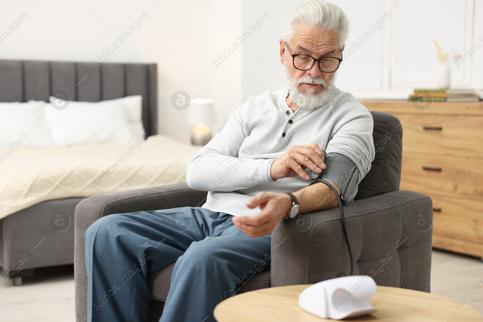 Photo of Senior man measuring blood pressure in armchair at home