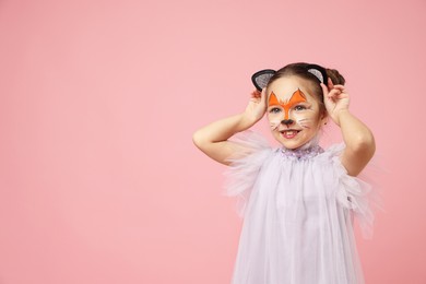 Photo of Cute girl with painted face and ears as cat on pink background, space for text