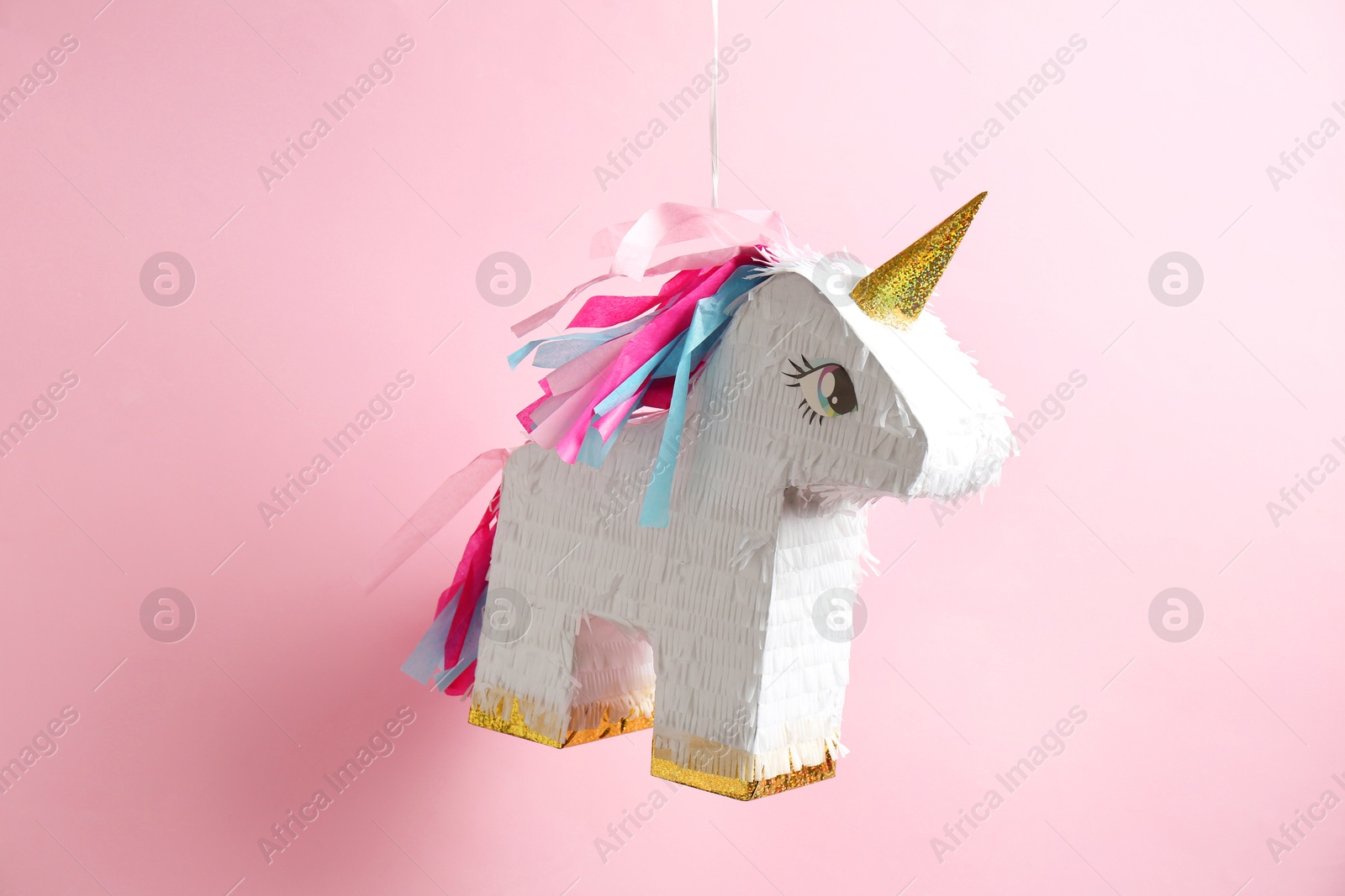 Photo of Bright pinata in shape of unicorn hanging on pink background