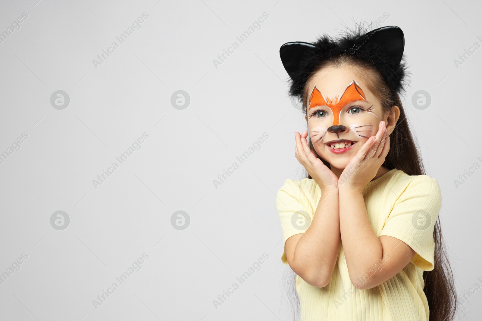 Photo of Cute girl with painted face and ears as cat on grey background, space for text