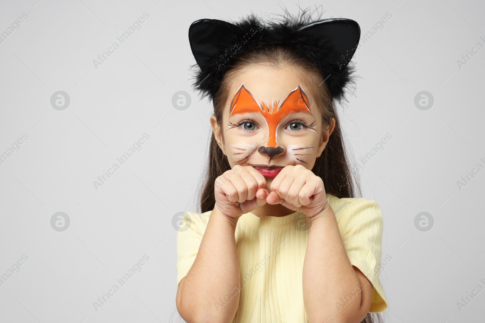 Photo of Cute girl with painted face and ears as cat on grey background, space for text