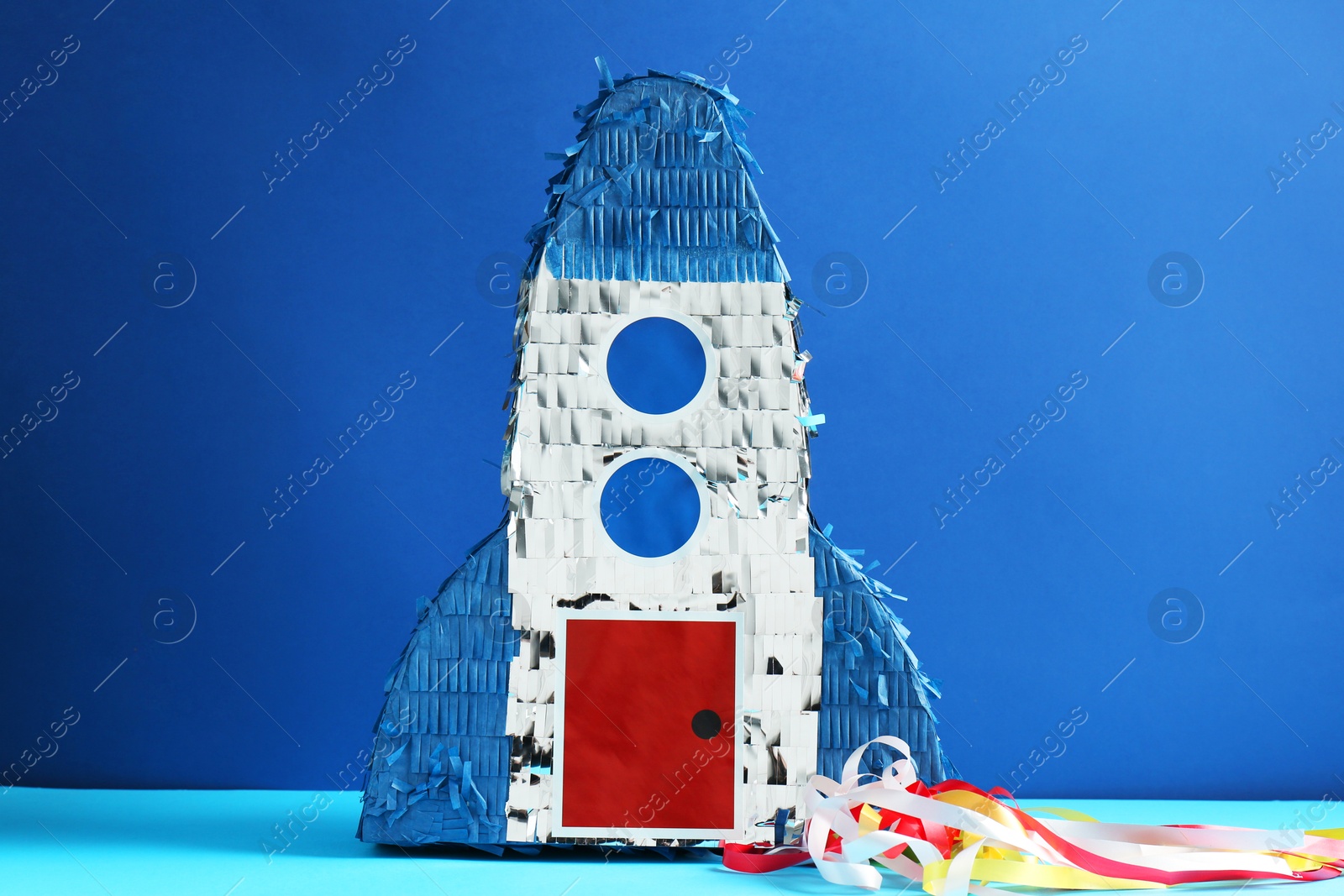 Photo of Bright pinata in shape of spaceship on blue background