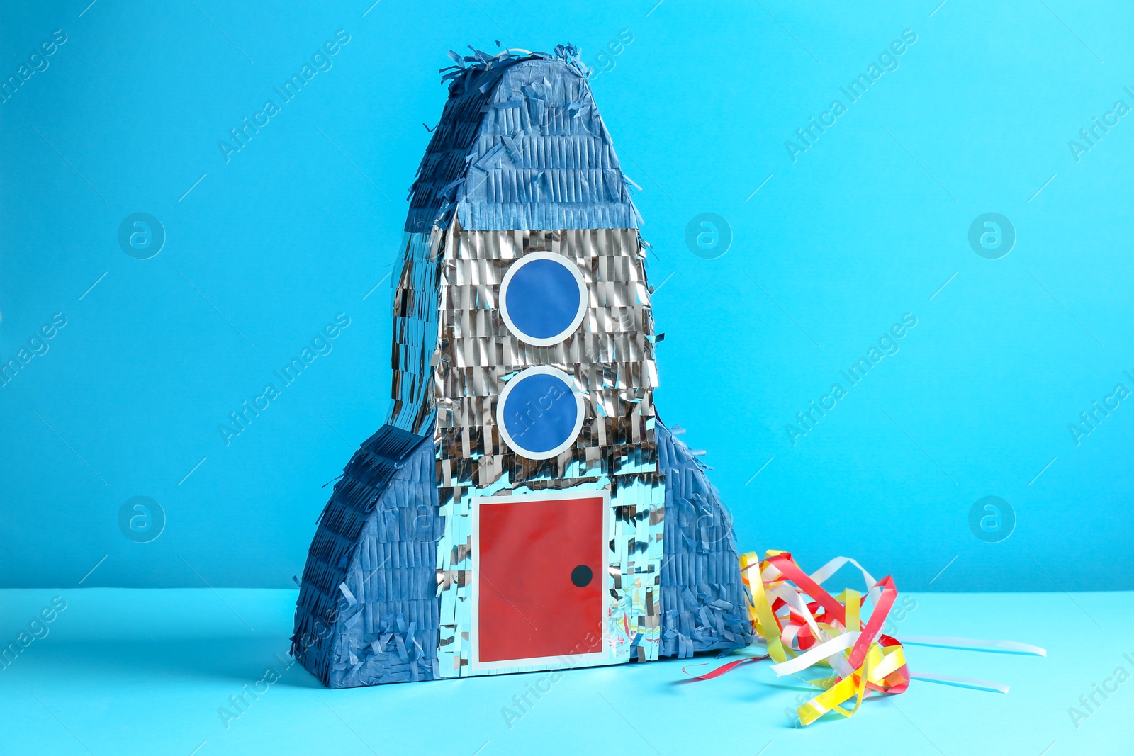 Photo of Beautiful pinata in shape of rocket on blue background