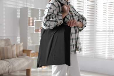 Photo of Woman with blank black shopper bag indoors, closeup. Mockup for design