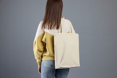 Photo of Woman with blank shopper bag on grey background, back view. Mockup for design