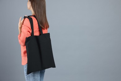 Photo of Woman with blank black shopper bag on grey background, back view. Mockup for design