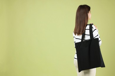 Photo of Woman with blank black shopper bag on color background, back view. Mockup for design