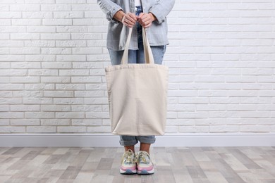 Photo of Woman with blank shopper bag near white brick wall, closeup. Mockup for design