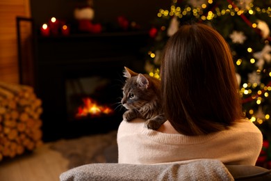 Photo of Woman with cute cat in room decorated for Christmas, back view. Space for text