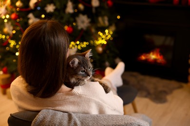 Woman with cute cat in room decorated for Christmas, back view. Space for text