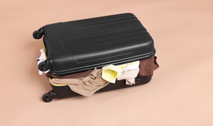 Photo of Packed suitcase full of clothes on beige background