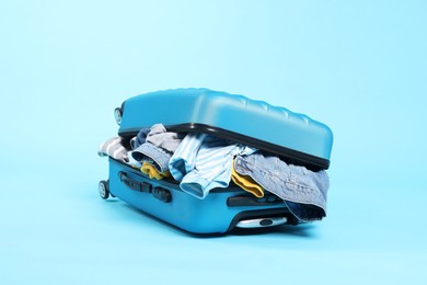 Photo of Packed suitcase full of clothes on light blue background