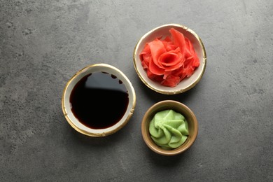 Photo of Hot wasabi paste, soy sauce and ginger on grey textured table, flat lay