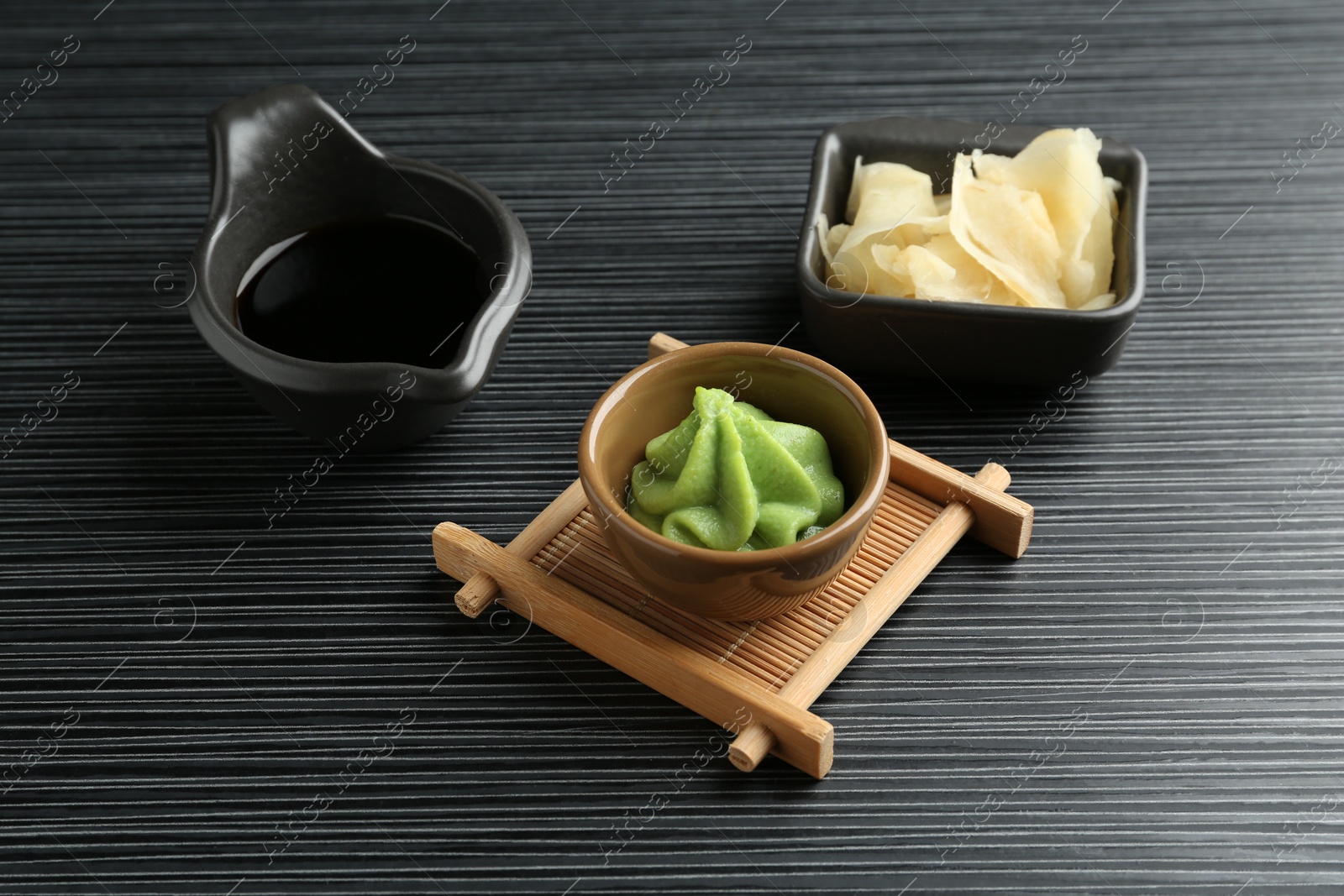 Photo of Hot wasabi paste, soy sauce and ginger on black textured table