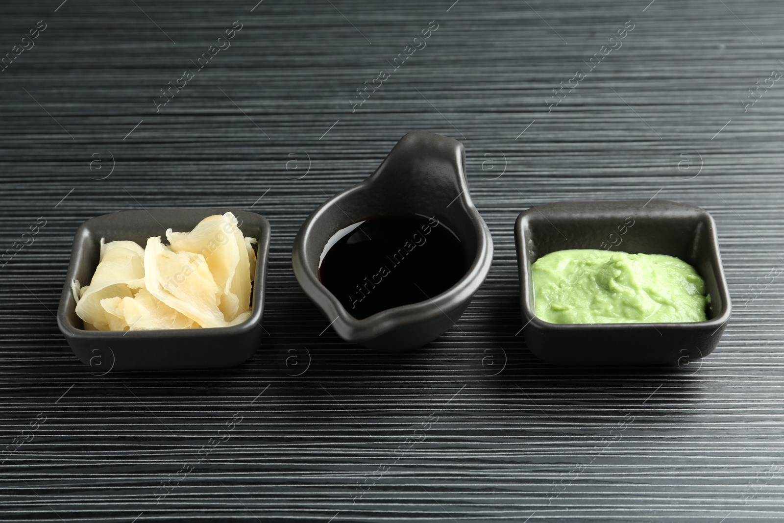 Photo of Hot wasabi paste, soy sauce and ginger on black textured table, closeup