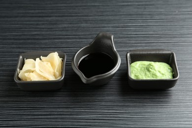 Photo of Hot wasabi paste, soy sauce and ginger on black textured table, closeup