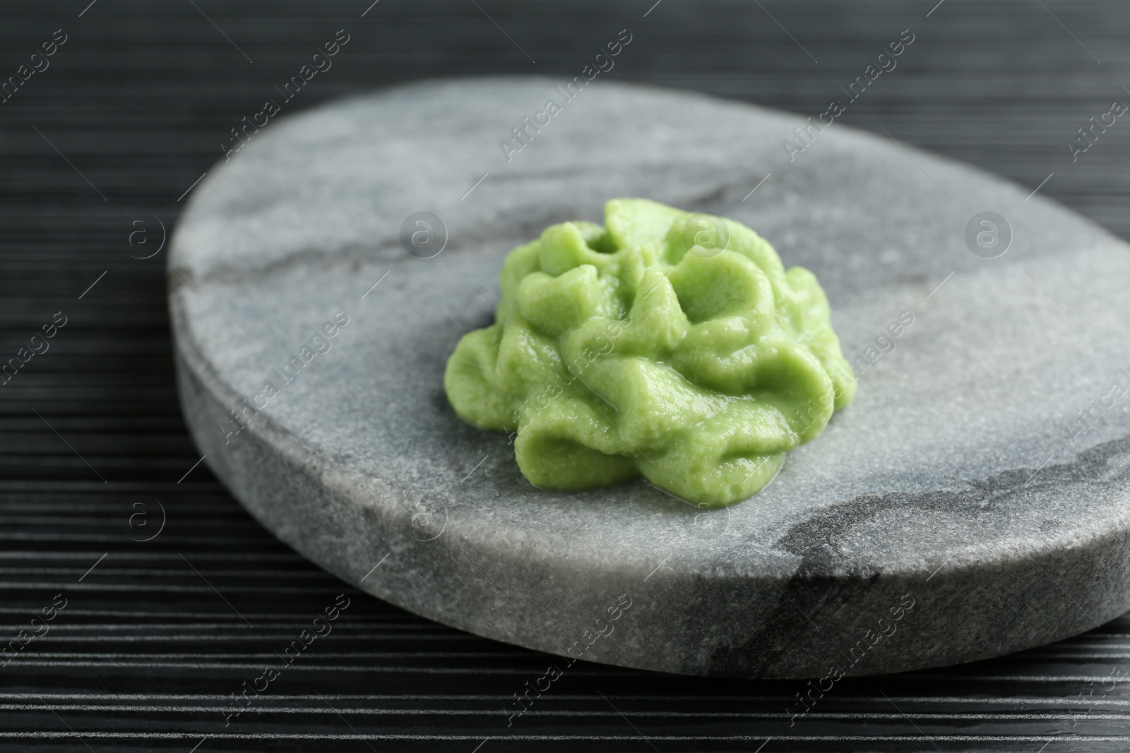 Photo of Marble board with hot wasabi paste on black textured table, closeup