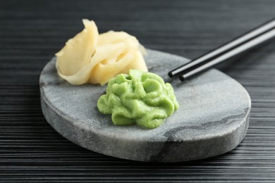 Photo of Marble board with hot wasabi paste, ginger and chopsticks on black textured table, closeup