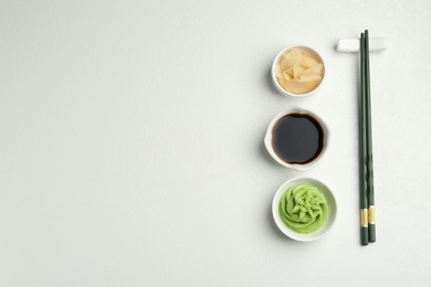 Photo of Hot wasabi paste, soy sauce, ginger and chopsticks on light textured table, flat lay. Space for text