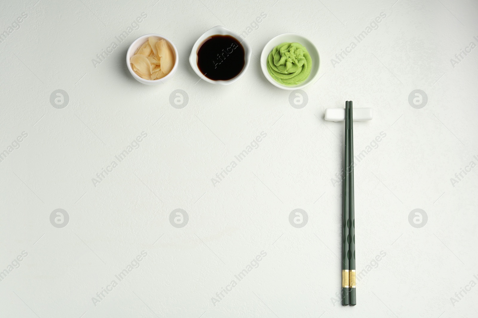 Photo of Hot wasabi paste, soy sauce, ginger and chopsticks on light textured table, flat lay. Space for text