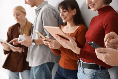 Photo of Group of people using different gadgets near light wall indoors. Modern technology