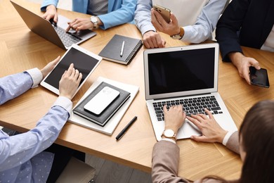 Photo of Group of people using different gadgets at wooden table in office, closeup. Modern technology