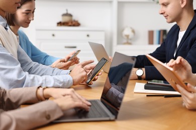 Photo of Group of people using different gadgets at wooden table in office. Modern technology