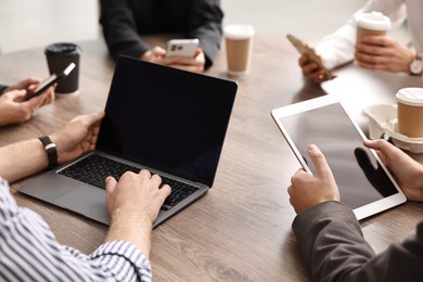 Photo of Group of people using different gadgets at wooden table in office, closeup. Modern technology