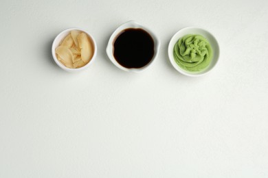 Photo of Hot wasabi paste, soy sauce and ginger on light textured table, flat lay. Space for text