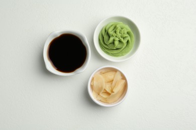 Photo of Hot wasabi paste, soy sauce and ginger on light textured table, flat lay