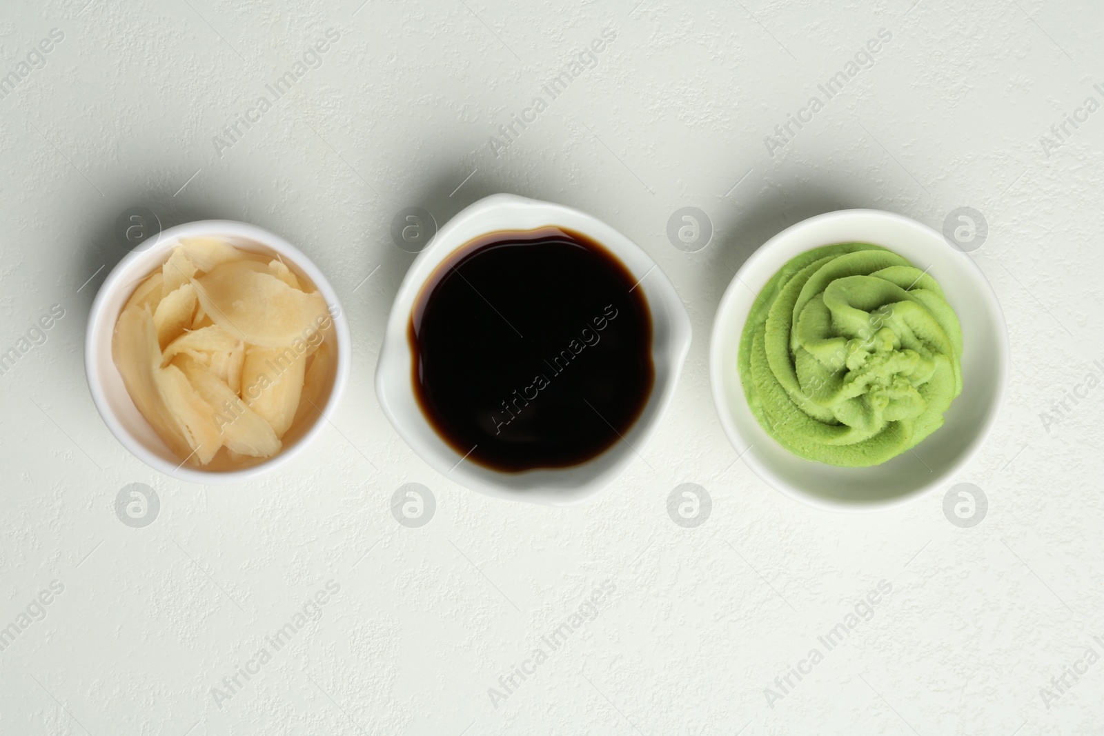 Photo of Hot wasabi paste, soy sauce and ginger on light textured table, flat lay