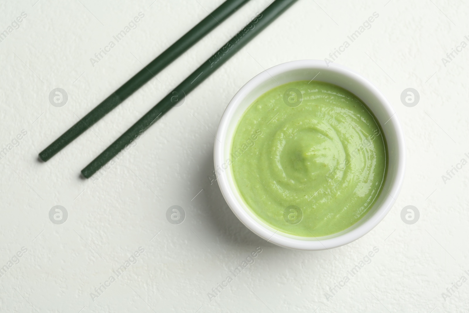 Photo of Hot wasabi paste in bowl and chopsticks on light textured table, top view