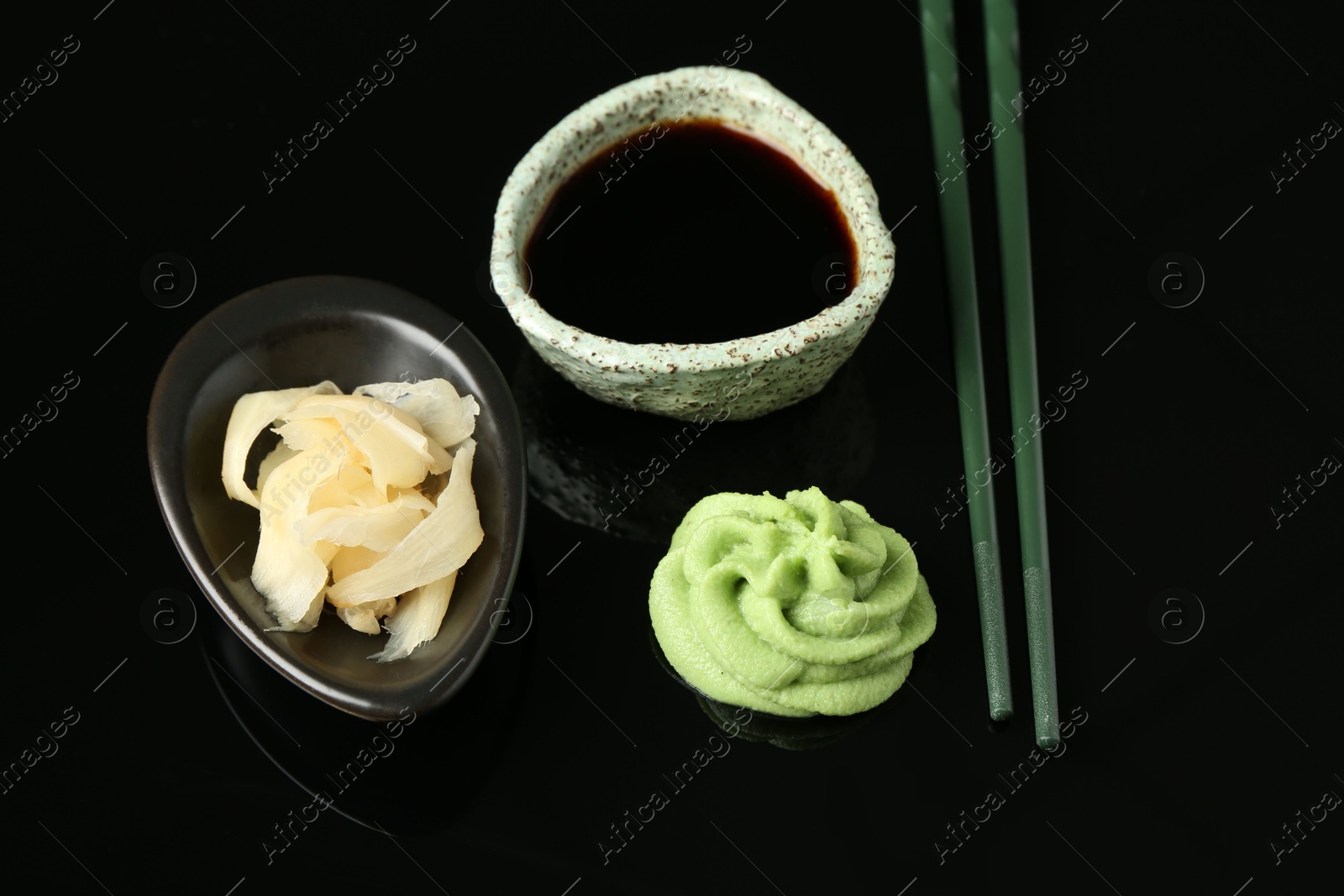 Photo of Hot wasabi paste, soy sauce, ginger and chopsticks on black mirror surface, above view