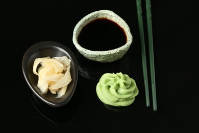 Photo of Hot wasabi paste, soy sauce, ginger and chopsticks on black mirror surface, above view