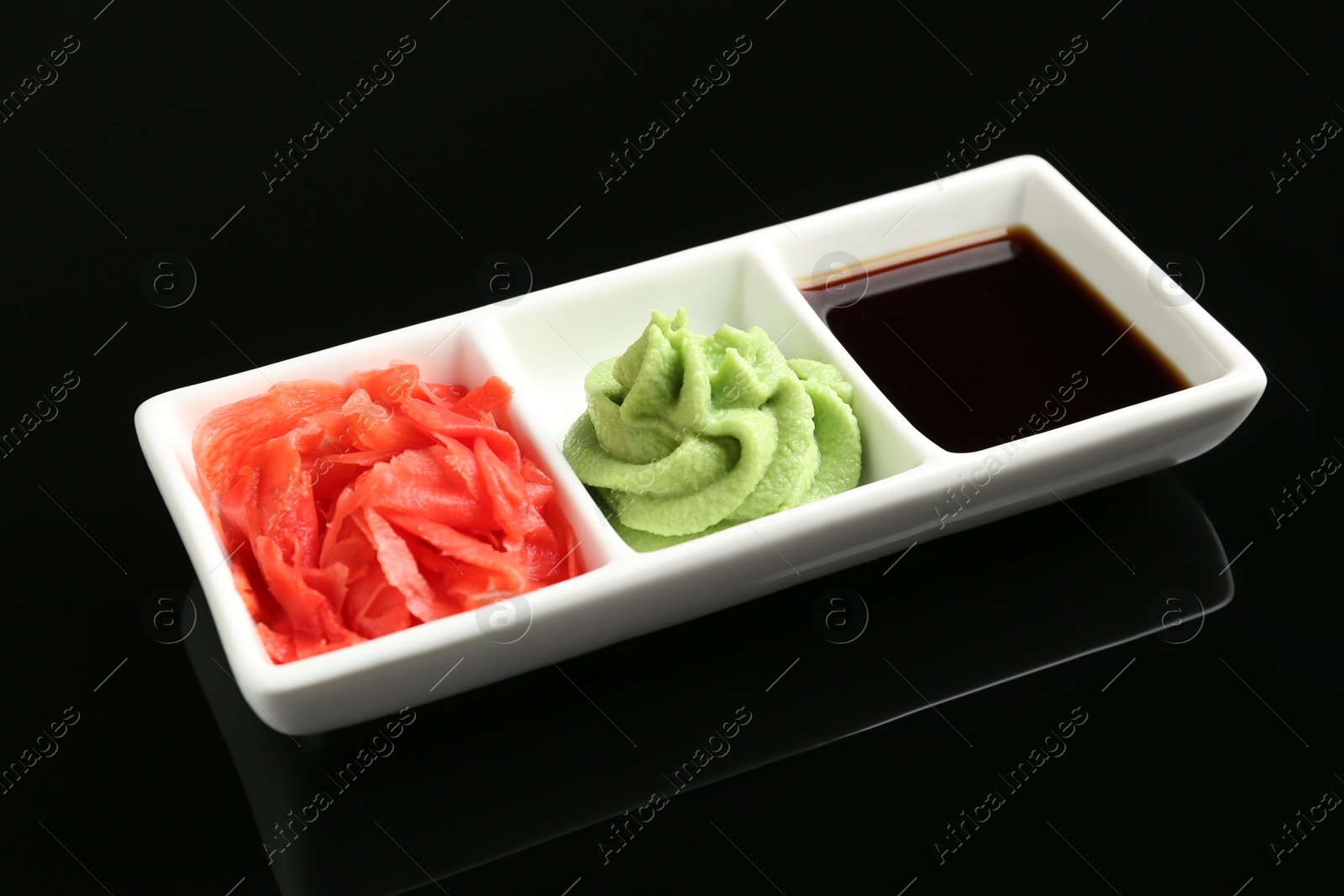 Photo of Hot wasabi paste, soy sauce and ginger on black mirror surface, closeup