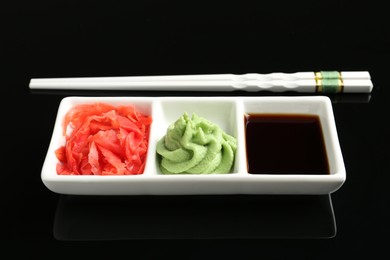 Photo of Hot wasabi paste, soy sauce, ginger and chopsticks on black mirror surface, closeup