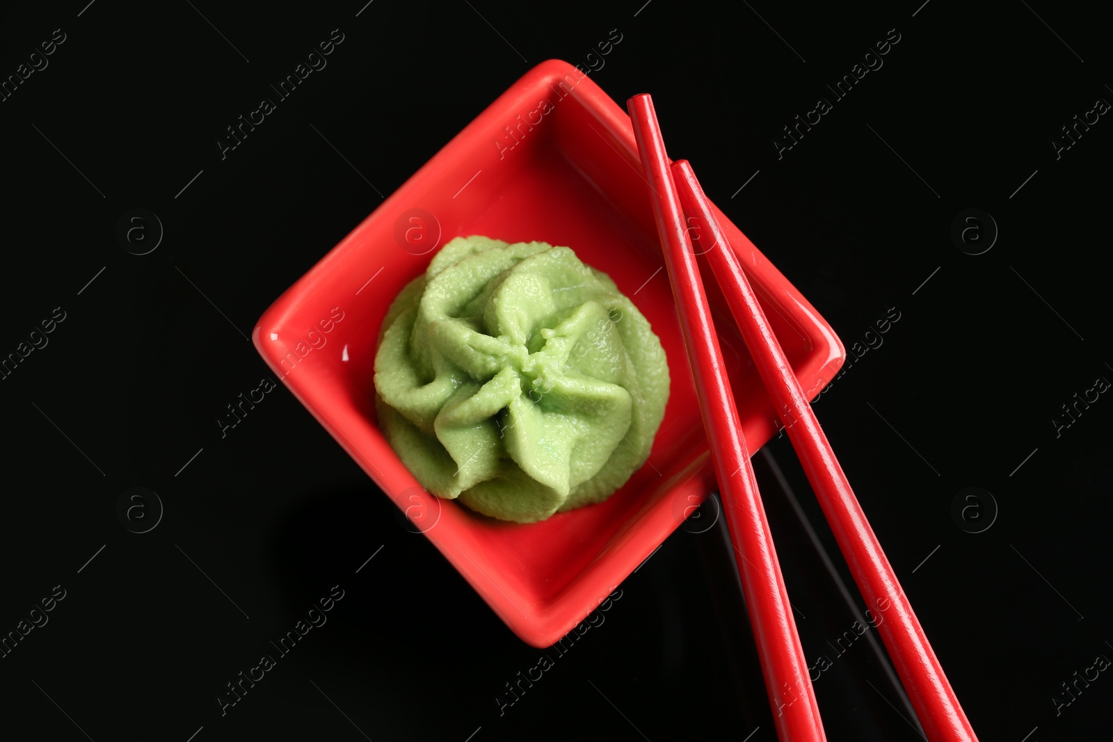 Photo of Hot wasabi paste in bowl and chopsticks on black background, top view