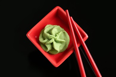 Photo of Hot wasabi paste in bowl and chopsticks on black background, top view