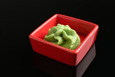 Photo of Hot wasabi paste in bowl on black mirror surface, closeup